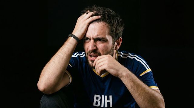 Frustrated soccer fan clutching head in bih jersey reacting to tense match result