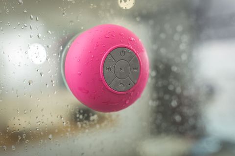 Waterproof pink bluetooth suction shower speaker sticking to wet glass with droplets