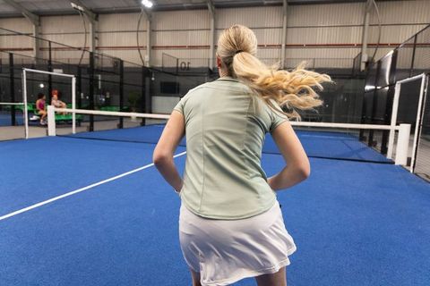 Female padel player moving toward net on blue indoor court during training session