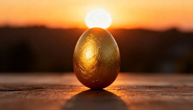 Golden egg reflecting sunset light on wooden surface casting long shadow and halo