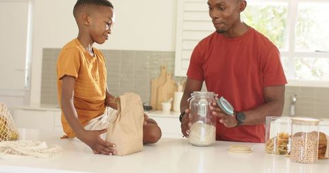 Father and son organizing pantry with glass jars and grains on kitchen counter