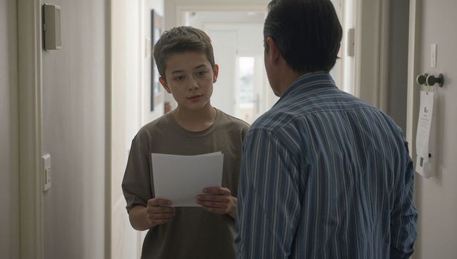 Teen Holding Documents in Hallway Facing Parent During Serious Conversation