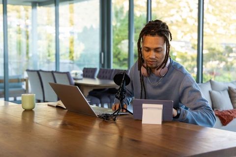 African American creator recording podcast at home studio with laptop tablet mic pink headset
