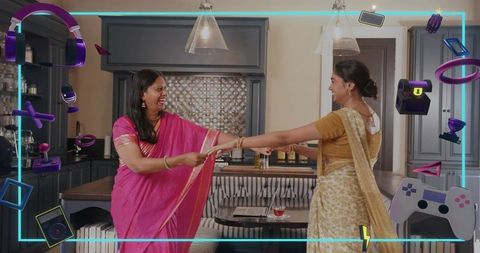 Indian mother and daughter laughing while holding hands in modern kitchen wearing sarees