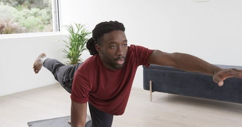 African American man performing single-leg bird-dog on yoga mat in sunlit living room