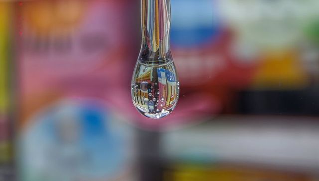 Macro droplet refracting colorful packaging labels while hanging from clear tube and bokeh