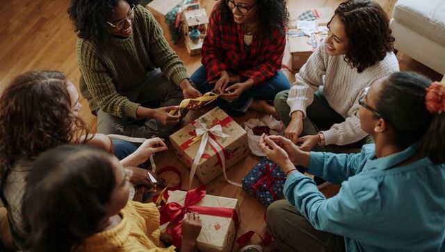 Friends wrapping gifts in cozy living room circle sharing ribbons and warm holiday cheer