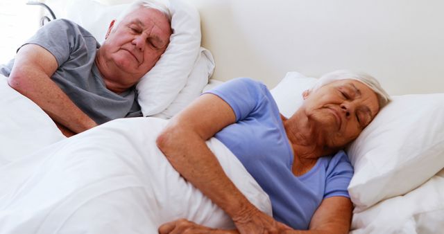 Elderly couple sleeping side by side on bed, covered with white blankets. Perfect for depicting themes of companionship, senior health, home life, comfort, and peaceful rest. Useful for articles, presentations, or advertisements related to elderly care, health and wellness, sleep solutions, and retirement living.
