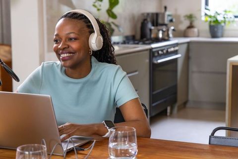 Female podcaster hosting remote podcast from bright minimal kitchen, smiling and recording