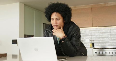 African American man leaning over laptop on modern kitchen countertop, concentrating on work