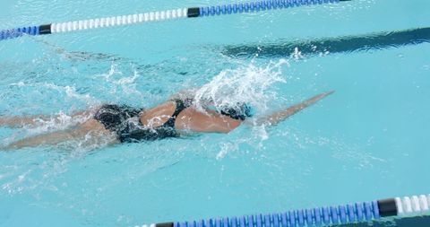 Depicts female swimmer performing freestyle stroke in pool, emphasizing strength and technique. Ideal for use in sports publications, fitness advertising, or content about swimming techniques and athletic training.