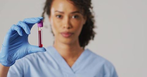 Asian technician holding blood vial wearing blue gloves and scrubs examining sample