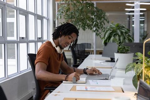African american professional writing notes at laptop in sunlit modern coworking space