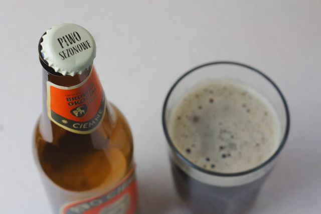 Photograph displays a close-up view of a beer bottle with a cap on and a glass of frothy dark beer. Ideal for use in advertisements, articles, and marketing materials related to brewing, beer culture, alcohol, and beverage promotions. Can also be used by pubs, bars, and restaurants to highlight their beer selection.