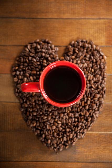 Coffee cup with heart shaped coffee beans on wooden table
