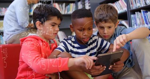 Diverse boys collaborating on tablet in library setting