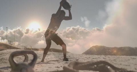 Man Training with Kettlebell on Beach Amidst Beautiful Clouds