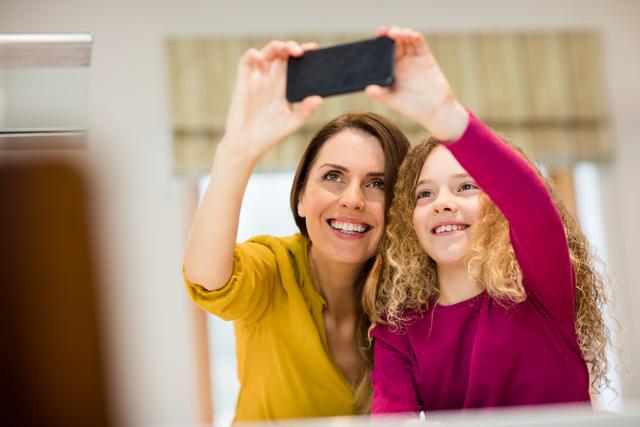 Mother and daughter taking selfie from mobile phone in kitchen at home