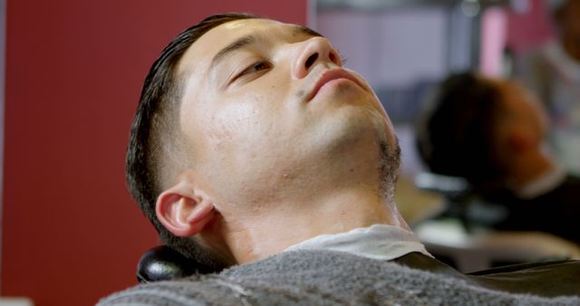 Image shows a man reclining in a barbershop chair, preparing for a haircut or grooming services. Ideal for use in promotions and advertisements for barbershops, grooming products, and men's self-care services.