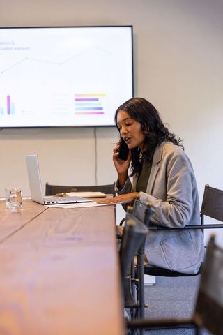 African american businesswoman talking on phone analyzing charts in modern meeting room