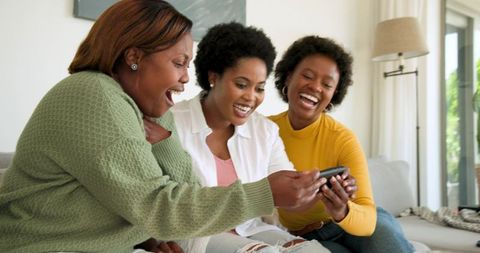 Three Friends Laughing at Shared Smartphone on Sofa at Home