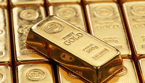 Polished 500g gold bar sliding across stack of bullion reflecting warm showroom light