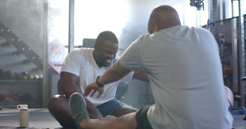African Men Laughing and Stretching on Gym Mat During Partner Workout