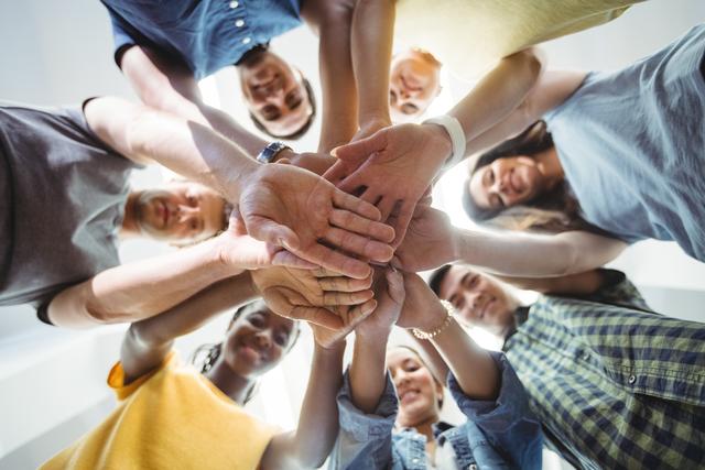 Group of diverse business executives stacking hands in a show of unity and teamwork. Ideal for illustrating concepts of collaboration, support, and team spirit in corporate environments. Perfect for use in business presentations, team-building workshops, and motivational materials.