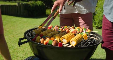 Friends Grilling Corn and Vegetable Skewers in Garden BBQ Gathering