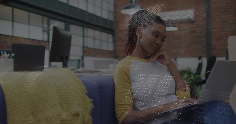 Professional woman working on laptop on blue sofa in modern industrial office lounge