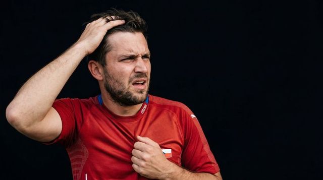 Exhausted male athlete in red jersey rubbing hair, catching breath, showing weariness