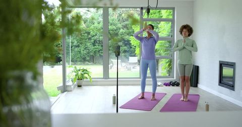 African women practicing yoga on purple mats in bright home studio with garden view