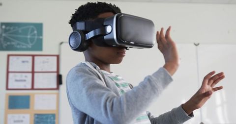 African American Boy Wearing VR Headset Interacting with Virtual Objects in Classroom
