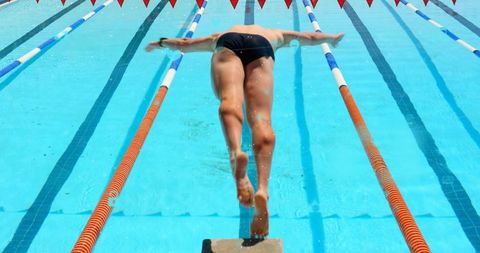 Diving Male Swimmer Launching from Starting Block into Sunlit Outdoor Pool