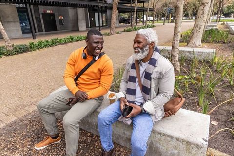 African american friends laughing and sharing smartphone over coffee in urban plaza