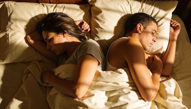 Couple sleeping back-to-back in warm morning sunlight conveying quiet distance