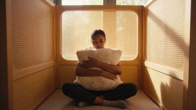 Sunlit cozy alcove woman sitting hugging fluffy pillow in rattan cubby for relaxation