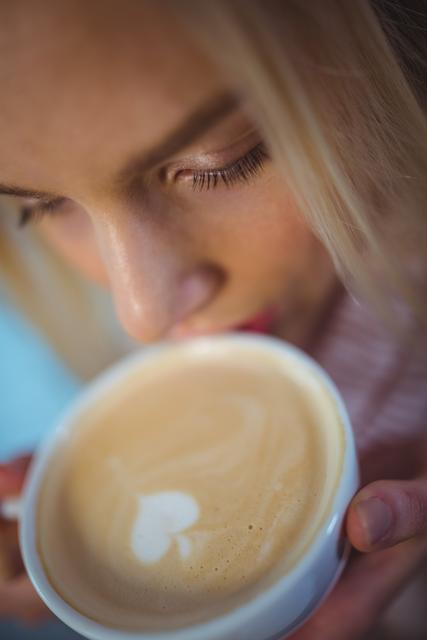 Close-up of a woman enjoying a latte with a heart design in a cozy cafe. Perfect for use in lifestyle blogs, coffee shop promotions, relaxation and leisure content, or advertisements for cafes and coffee products.