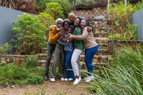 Multigenerational african american family hugging in backyard garden on stone steps