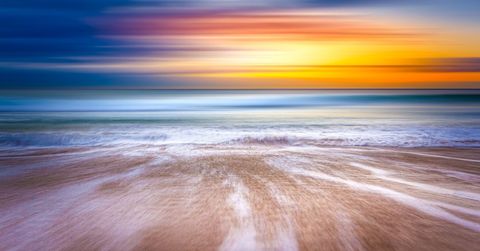 Waves washing over sandy shore at colorful sunset with horizontal motion blur