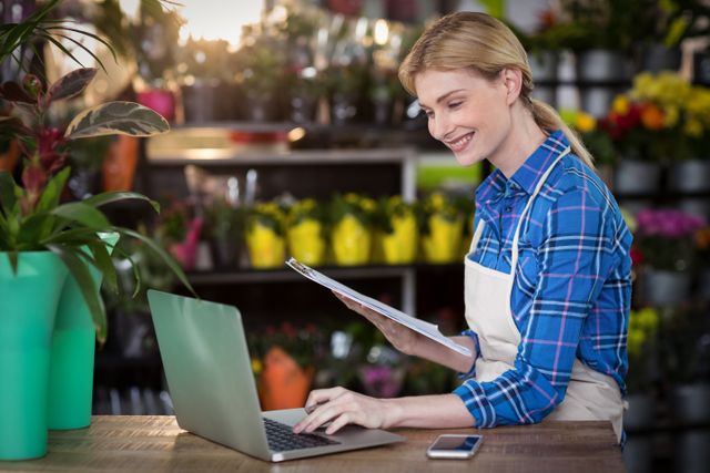 Female florist using laptop while holding clipboard in the flower shop