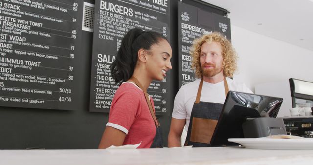 Happy diverse male and female baristas wearing aprons talking behind the coiunter in cafe. Local business owner and hospitality concept.