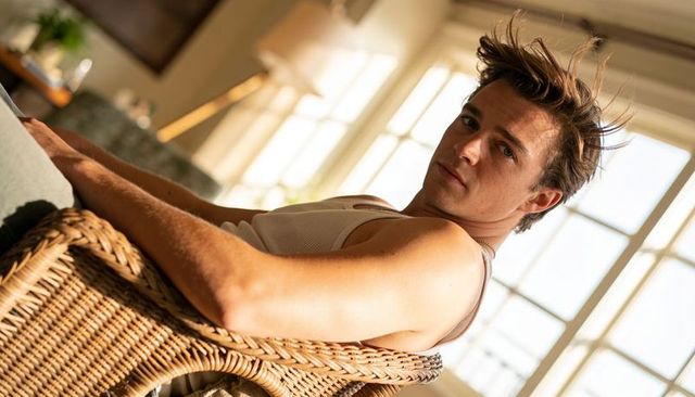 Sunlit young man reclining in wicker chair wearing beige ribbed tank top