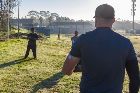 Morning baseball teammates practicing catch on grassy field with midair ball and gloves