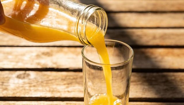 Sunlit orange juice pouring from glass bottle into tall glass on rustic wooden table