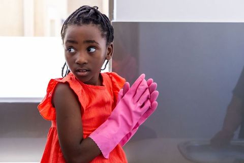 Thoughtful girl wearing pink rubber gloves standing by modern kitchen sink in red dress