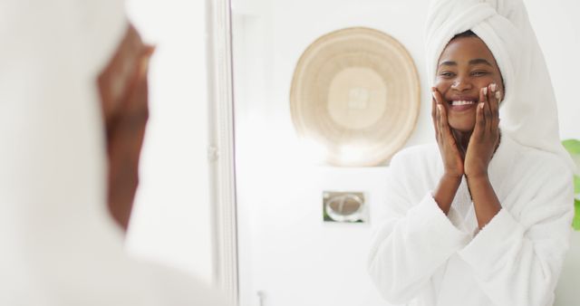 Image of happy african american woman in robe looking at mirror and moisturizing face - Download Free Stock Photos Pikwizard.com