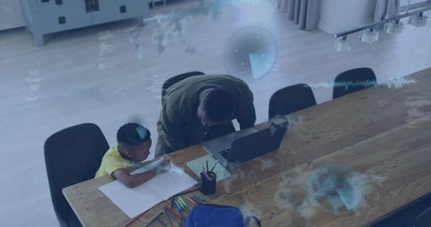 Parent leaning over helping child studying at dining table using laptop and colored pencils