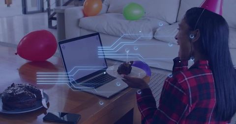 Young woman celebrating virtual birthday with cake and laptop in cozy living room party