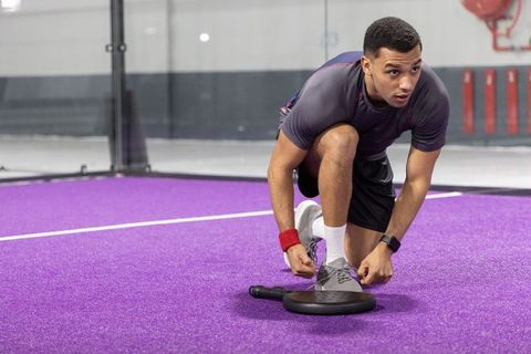 African american athlete kneeling tying shoe on purple paddle court preparing for match